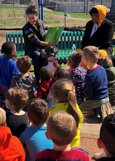 Volunteer with foster dog reading to children